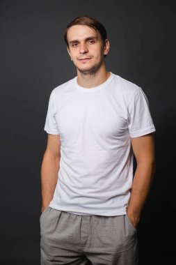 Beyaz tişörtlü yakışıklı genç bir adam gri bir arka planda duruyor. Yazıt için giysiler. maketleme