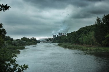 Çevre kirliliği kavramı. Fabrikanın bacasından çıkan duman doğayı öldürüyor. Kasvetli sanayi manzarası. Nehir ve orman