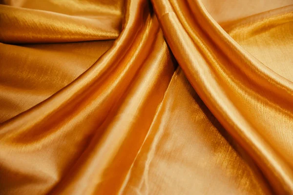 Een gouden gerimpelde stof ligt in vouwen op een gedrapeerde tafel. — Stockfoto