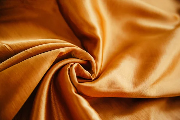 Ett gyllene rynkigt tyg ligger i veck på ett draperat bord. Stockbild