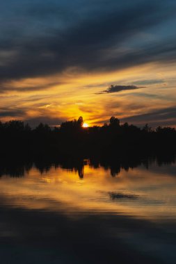 Atmospheric sunset behind trees and reflection in water.