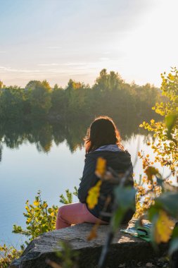 Kız gölün yakınındaki bir kayanın üzerinde tek başına oturuyor..