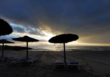 Saman plajı şemsiyeleri, İspanyol sahilinde gün batımı.