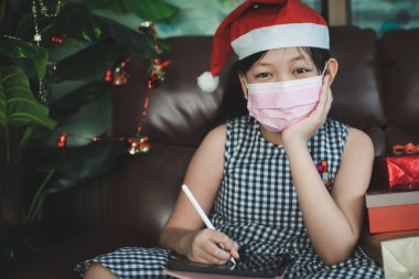Asyalı bir kız başkaları için iyi şeyler yazmayı düşünüyor. Maske takan bir kız Noel ve yeni yıl boyunca yazmak için tablet kullanır.