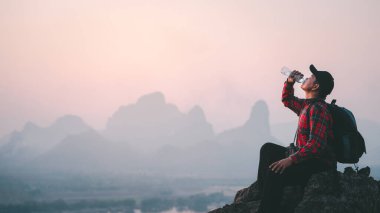 Başarılı bir yürüyüşçü dağın tepesinde uçurumun kenarında su içer. Macera yolculuğu kavramı.