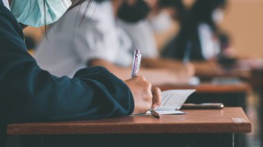 Koronavirüs acil durumu nedeniyle yüz maskesi takan öğrenci sınavına giriyor. Sınıfta oturan genç kadın Covid-19 salgınından dolayı cerrahi maske takıyor.