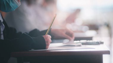 Koronavirüs acil durumu nedeniyle yüz maskesi takan öğrenci sınavına giriyor. Sınıfta oturan genç kadın Covid-19 salgınından dolayı cerrahi maske takıyor.