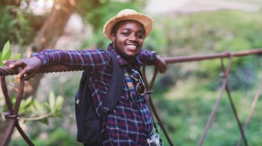 Sırt çantası ve film kamerasıyla gülümseyen Afrikalı gezgin milli parkta mutlu bir şekilde dinleniyor. Macera seyahati ve tatil kavramı