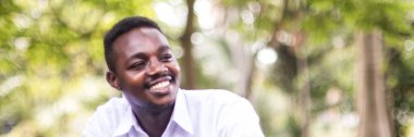 Beyaz gömlekli Afrikalı adam parkta mutlu bir şekilde oturup güler. Pozitif düşünce ve mutlu yaşam kavramı