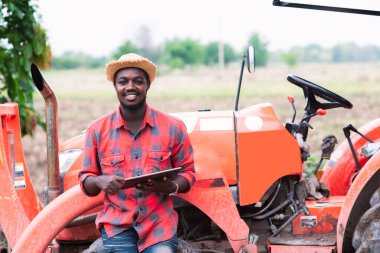 Afrikalı çiftçi tarlada traktörle çalışıyor ve tablet kullanıyor. Tarım yeniliği ve tarım kavramı