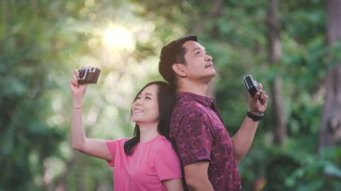 Asyalı çift parkın içinde klasik kamerayla doğanın fotoğraflarını çekiyor. Seyahat ve fotoğrafçılık kavramları.