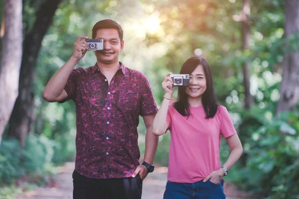 Asyalı çift parkın içinde klasik kamerayla doğanın fotoğraflarını çekiyor. Seyahat ve fotoğrafçılık kavramları.
