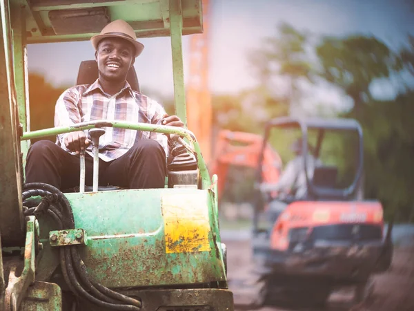 African man driving backhoe or operating excavator on construction site