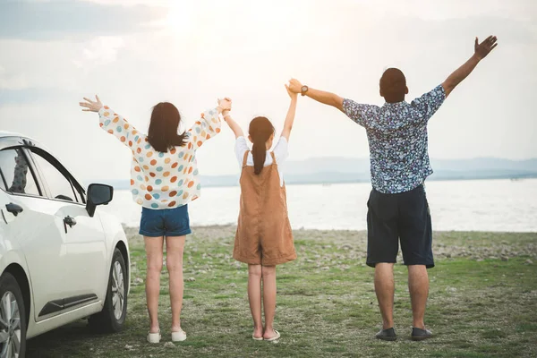 Back view of Freedom family father, mother and daughter having fun on a tropical beach and a car on the sider. Family vacation holiday and travel concept