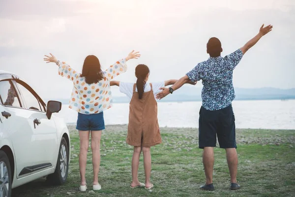 Back view of Freedom family father, mother and daughter having fun on a tropical beach and a car on the sider. Family vacation holiday and travel concept