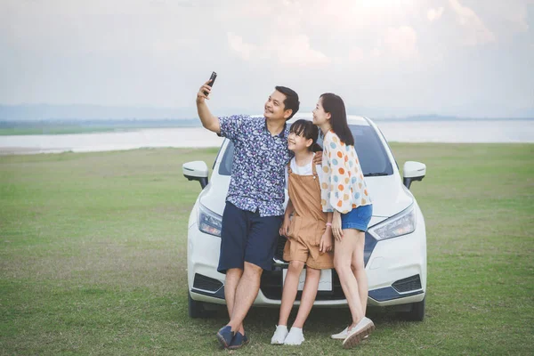Happy Family with father mother and daughter selfie and looking smartphone and having fun on a tropical beach and a car on the sider. Family vacation holiday and travel concept