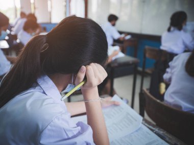 Students reading exam answer sheets exercises in classroom of school with headach