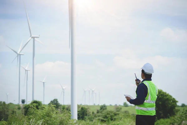 Engineer man stand holding tablet front the wind turbines generating electricity power station. Concept of sustainability development by alternative energy