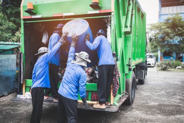 Çöp taşıma işçileri. Leş yiyiciler çöp kutusu alır. Erkekler çöp konteynırını çöp toplamak ve taşımak için arabaya doldururlar.