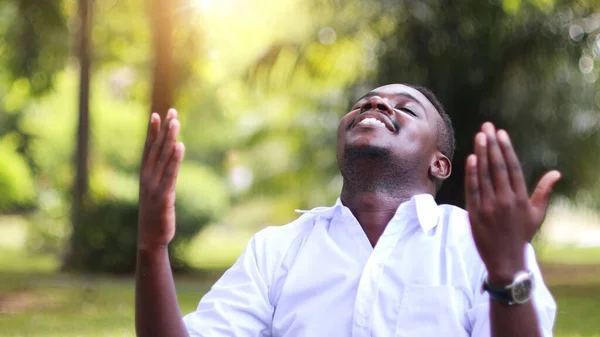 African man in white shirt praying for thank god in the green nature backgroun