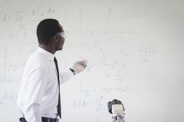 African teacher is explaining science lessons inside the classroom with a  scientific equations in background
