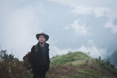 Sırt çantası taşıyan şapkalı özgürlük yolcusu sisli bir günde dağın tepesinde duruyor. Macera yolculuğu ve başarı kavramı.