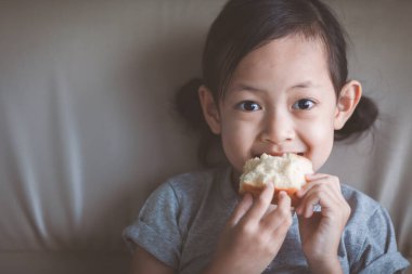 Parlak gözlü Asyalı kız mutlu bir şekilde ekmek yiyor. Sağlıklı yiyeceklerle çocuk konsepti..