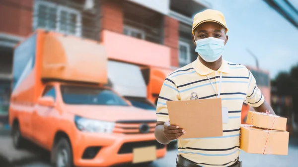 African delivery man in face mask holding a box package and cardboard .Concept of delivery service and consumer safety