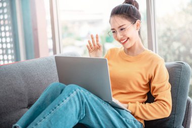 Mutlu Asyalı kadın, arkadaşıyla internetteki uygulamayla video konferans yapıyor, el sallıyor ve merhaba diyor.