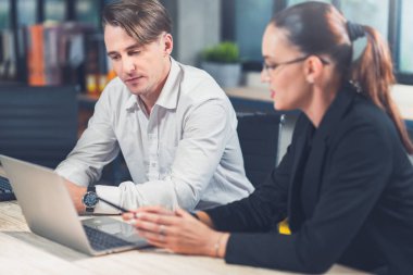 İki farklı iş adamı ofiste dizüstü bilgisayarın önünde sohbet ediyorlar. Erkek, fikirleri paylaşıyor ya da kadın iş arkadaşıyla iş kuruyor. İş planlaması.