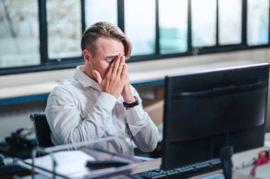 Stresli bir iş. Mutsuz genç erkek bilgisayar bilgisayarı, kriz ve girişimcilik konularında çalışma masasında oturuyor, baş ağrısı konsepti