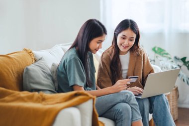 İnternetten alışveriş yapan iki mutlu ev arkadaşı. Kredi kartı ve dizüstü bilgisayarla birlikte evdeki bir kanepede oturuyorlar..