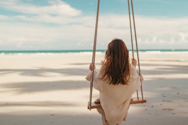 Freedom young resting woman enjoying feel, female sitting on swings near sea beach in sunshine. Summer relax.