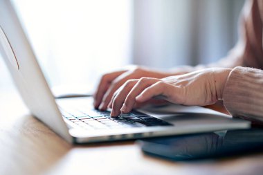 Evdeki ahşap masadaki dizüstü bilgisayarda çalışan ve dokunan bir kadının eli.