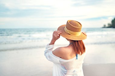 Summer beach vacation concept, Young woman with hat relaxing with her arms raised to her head enjoying looking view of beach ocean on hot summer day, copy space.
