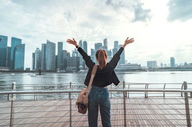 Arkaya bakan genç turist kadın kollarını kafasının üstüne kaldırmış Singapur şehrinin tadını çıkarıyor, her yere gidiyor, yaz tatili tatilinde