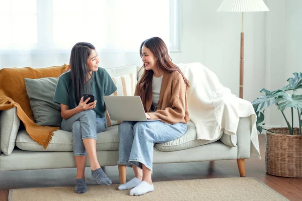 Two woman communicate with their friends and classmates via video link using a laptop and smartphone in the living room. Friends, friendship, time together