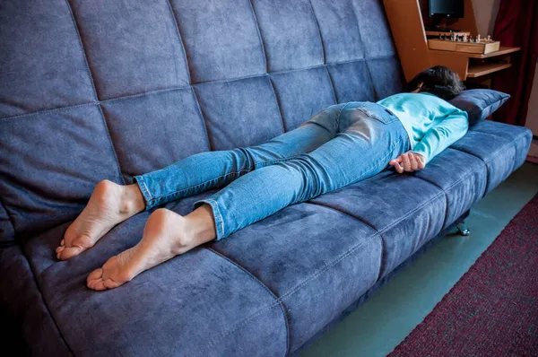 彼女の胃の上に横たわるソファの上で寝ているブルネットの女の子 — ストック写真