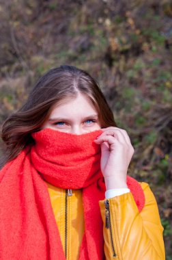 Uzun saçlı bir kız güneşli bir sonbahar gününde yüzünü turuncu bir eşarpla örttü.