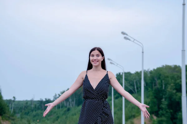 Szczęśliwa Dziewczyna Długimi Włosami Czarnej Sukience Stoi Drodze Ręce Boki — Zdjęcie stockowe