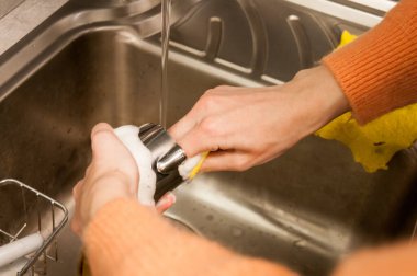 Bir kız kahve bardağında lavaboda kupa yıkıyor.