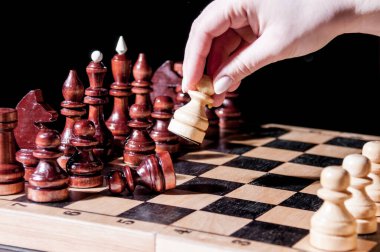 Beyaz piyonu olan bir kadının eli satranç tahtasındaki siyah piyonu deviriyor.