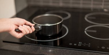 Mutfaktaki elektrikli tavayı koyan tencereyi tutan kadın..