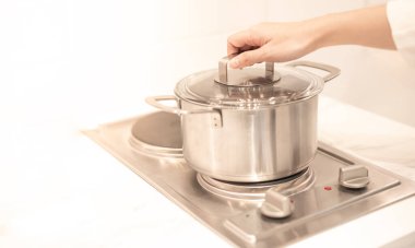 Kadın el, mutfaktaki elektrikli tavaya konan bir tencereyi tutuyor..