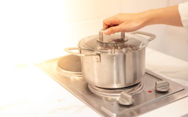 Kadın el, mutfaktaki elektrikli tavaya konan bir tencereyi tutuyor..