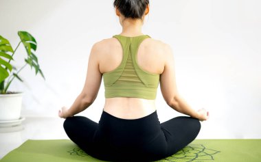 Kadın yoga dersleri alıyor, nefes alıyor, meditasyon yapıyor evdeki yeşil yoga minderinde oturuyor..