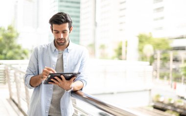 Genç adam ofis dışında çalışmak için bir tablet kullanır. Günlük kıyafet giyen, düşünceli ve ciddi bir adam..
