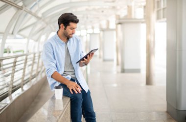 Genç adam ofis dışında çalışmak için bir tablet kullanır. Sıradan kıyafetler giyen, rahat ve mutlu hisseden adam..