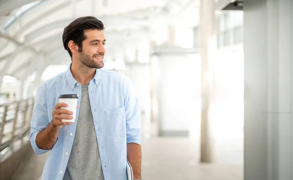 Young caucasian man holding cup of coffee and working on freelance project using portable computer at outer office.