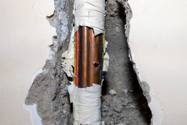 Etrafı çeşitli kablo ve borularla çevrili bir duvardaki hasarlı bakır boru.